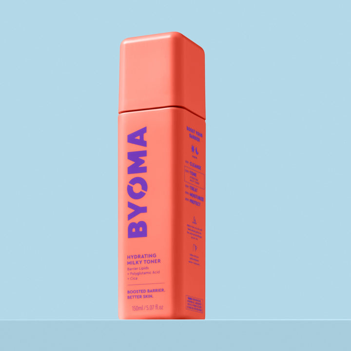 Une bouteille de tonique lacté hydratant Byoma, vue en angle montrant les étapes de routine « Boost Your Barrier » sur le panneau latéral, sur fond bleu.