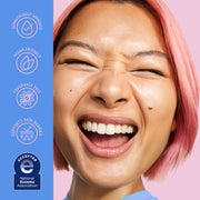 Gros plan d'une femme souriante aux cheveux roses sur fond rose, avec un panneau vertical bleu sur la gauche répertoriant des allégations telles que approuvé par les dermatologues, végétalien, sans parfum et soutient la barrière cutanée, ainsi qu'un badge d'association d'eczéma accepté.