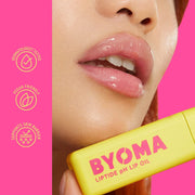 Huile à lèvres jaune avec la marque « BYOMA » détenue par une personne sur fond rose