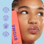 Femme tenant un produit de soin BYOMA avec des icônes de marque sur fond bleu clair